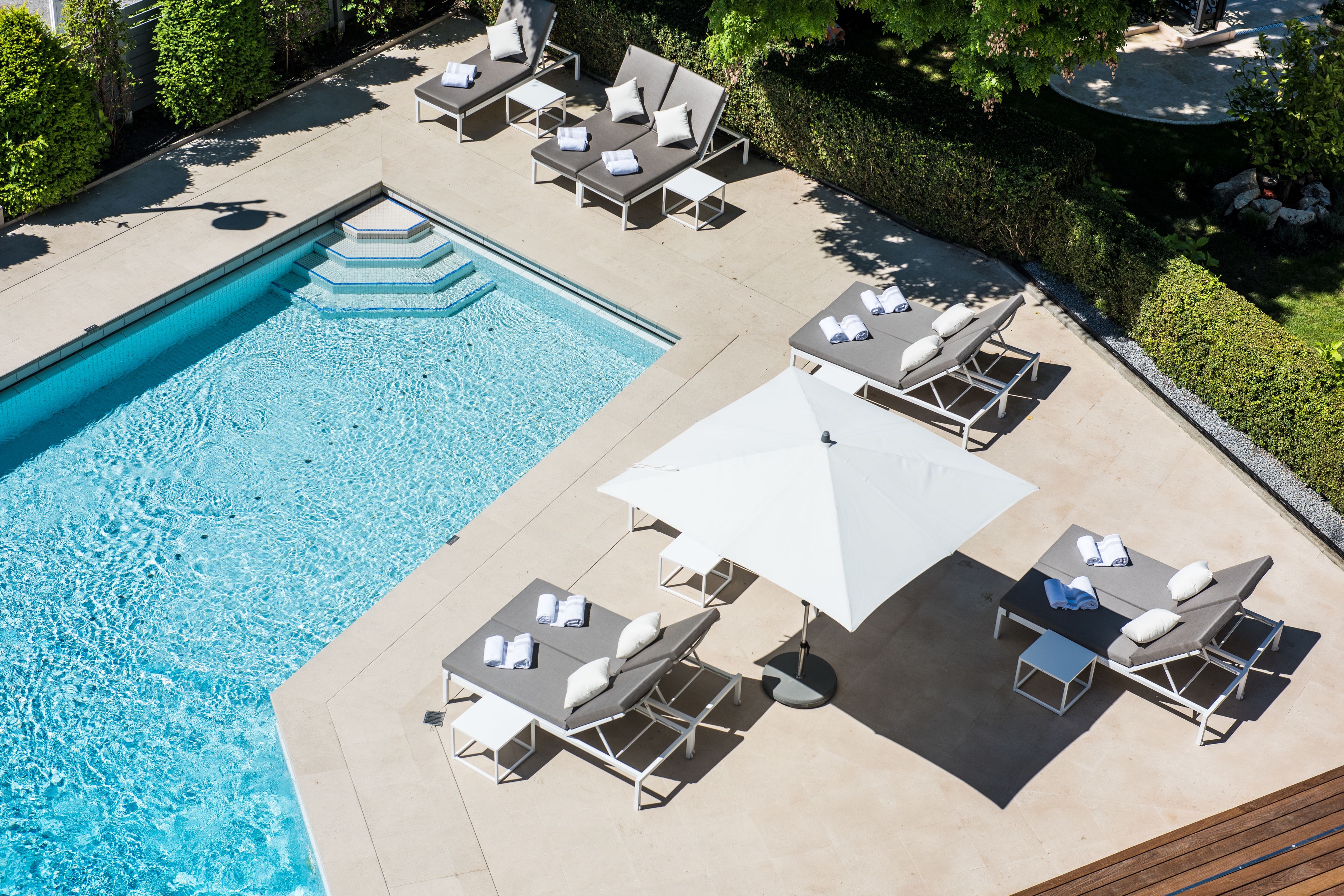 Uma área de piscina com espreguiçadeiras e uma mesa, cercada por um viveiro e árvores.
