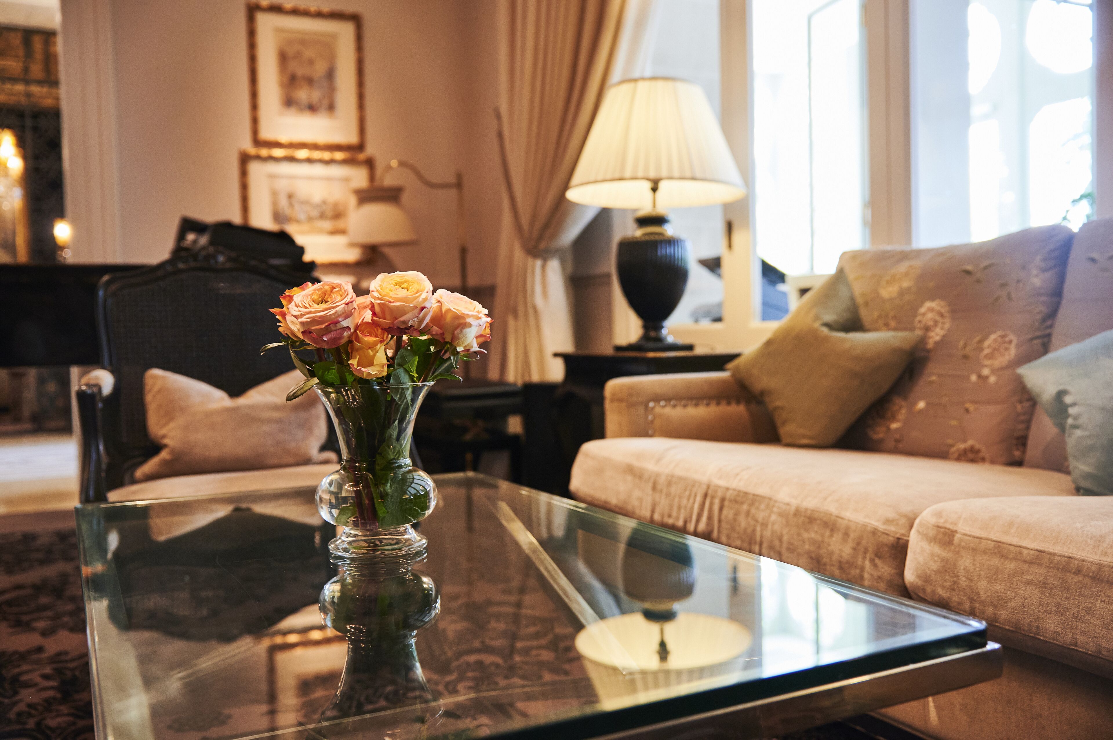 Un salon avec une table basse en verre, un vase de fleurs, un canapé et une lampe.