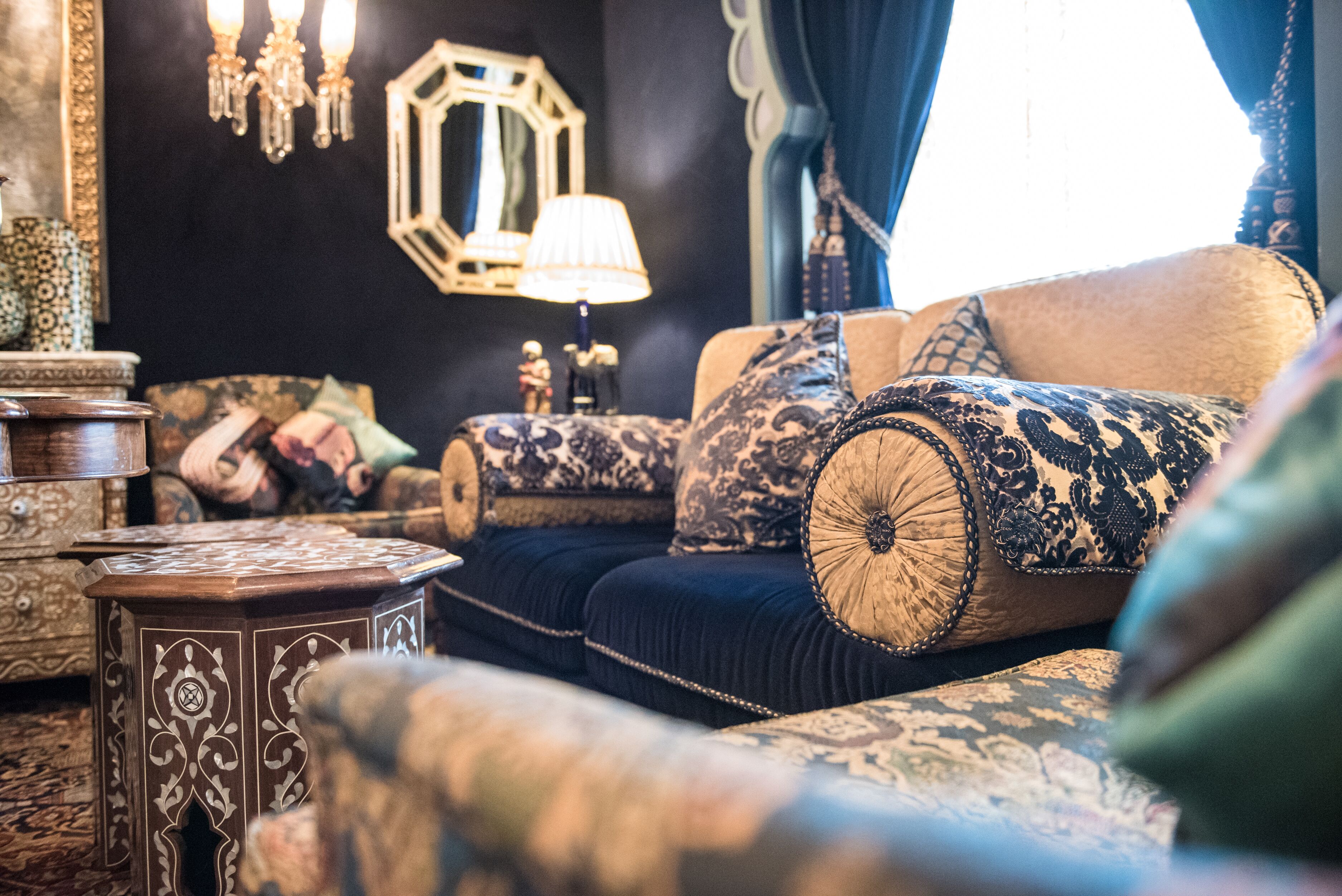 A traditional living room with a sofa set, patterned cushions, a side table, and a decorative mirror.