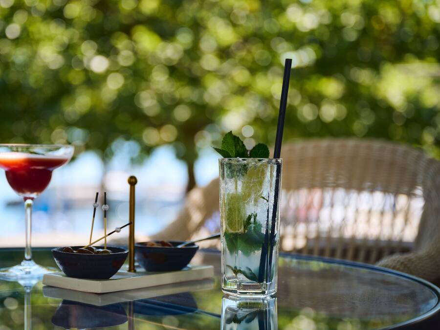 A glass table with a martini glass, a bowl with skewers, and a glass with a straw and mint leaves.