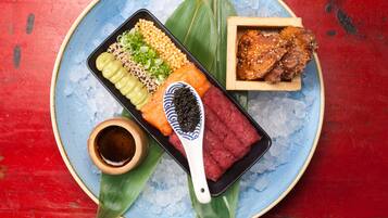 A traditional Japanese meal on a blue plate with ice, including sashimi, pickled vegetables, and a small bowl of soy sauce.
