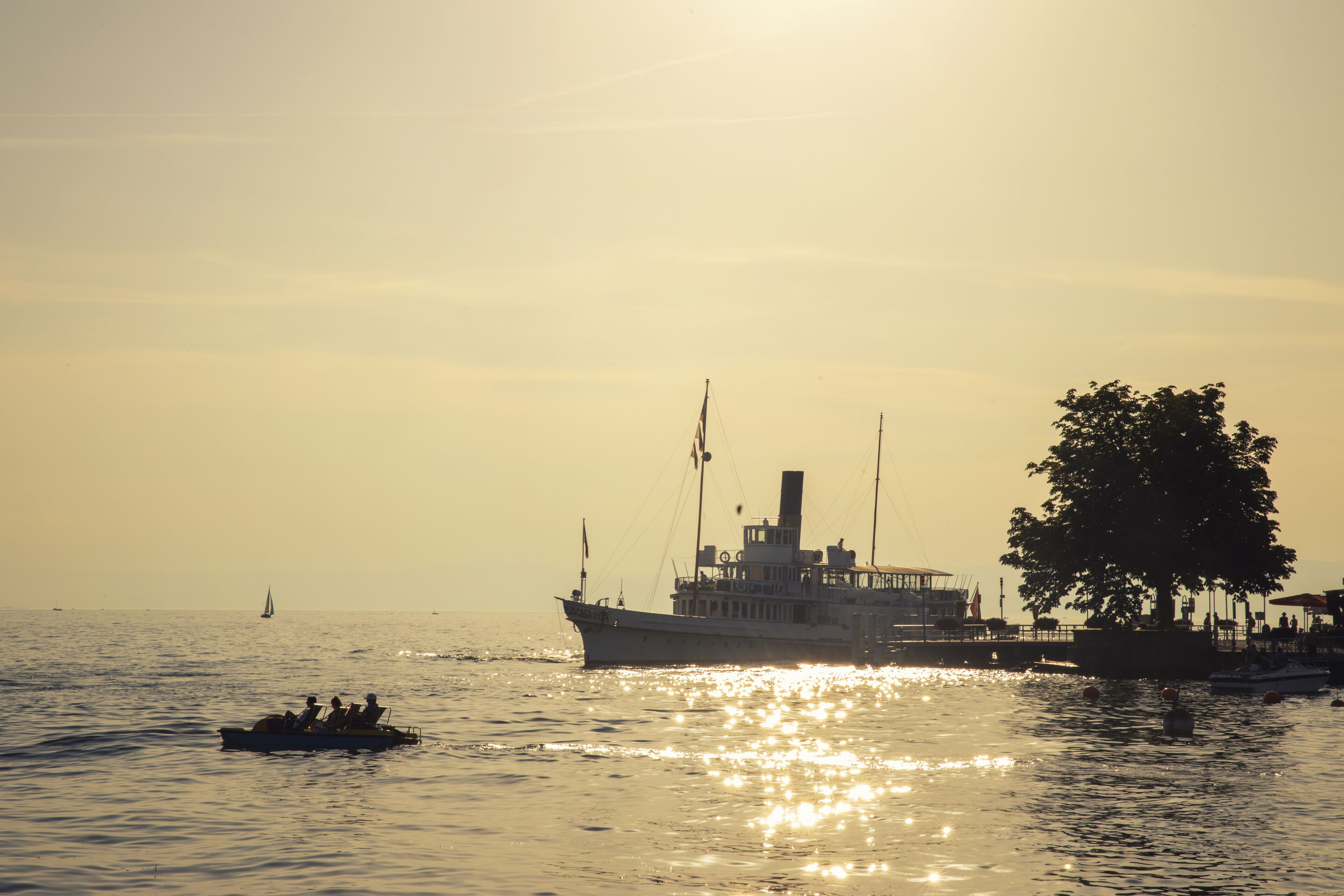 A boat with passengers and a docked ship, both on calm water.