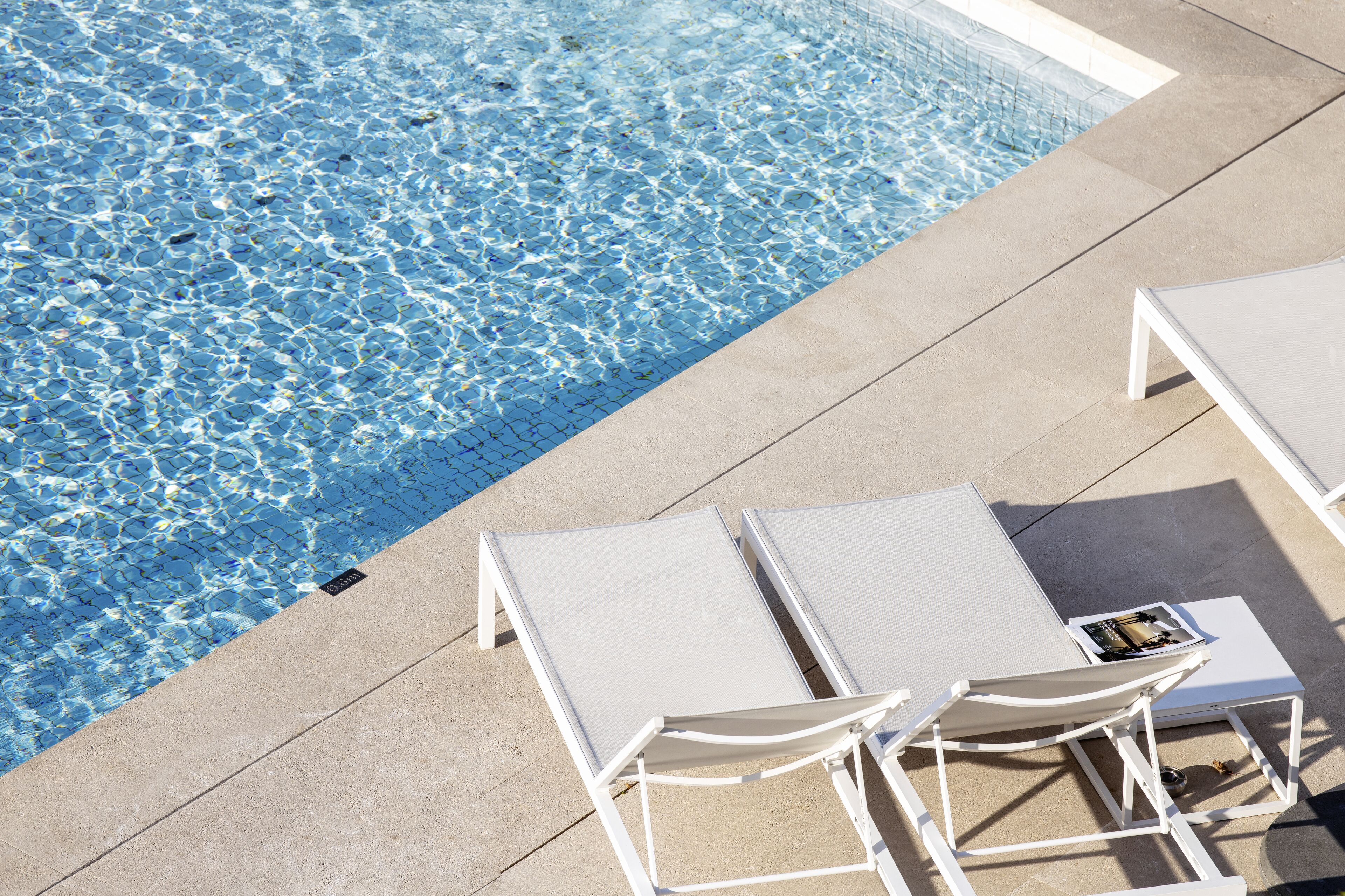 A poolside area with two white lounge chairs and a small table, surrounded by a tiled deck.