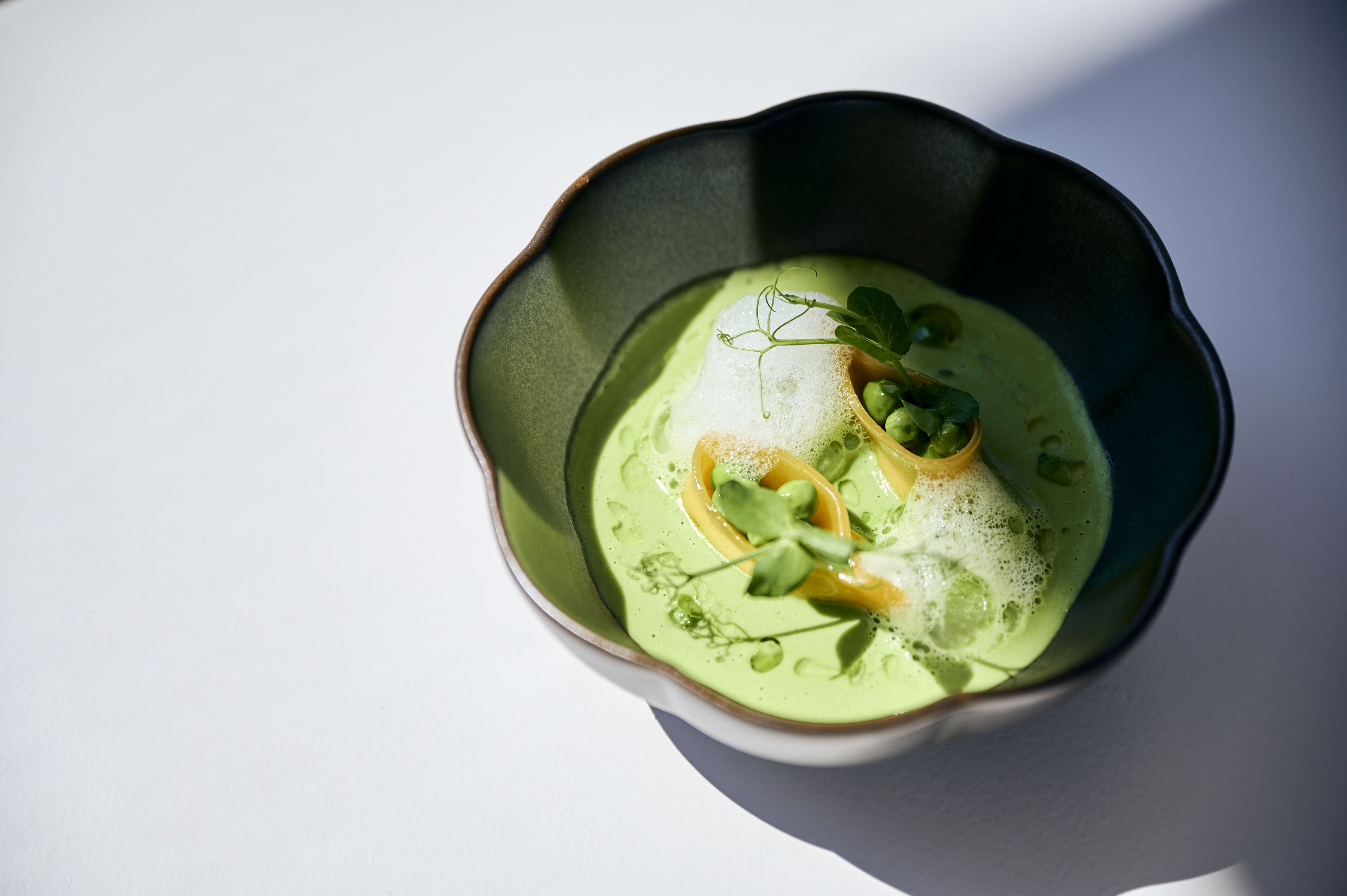 A bowl of green soup with a garnish, served in a dark bowl on a white surface.