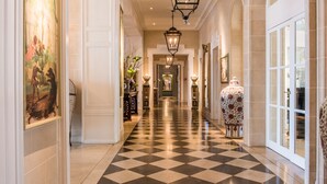 Un couloir d’hôtel avec un sol à carreaux, des décorations murales élaborées et un grand vase.