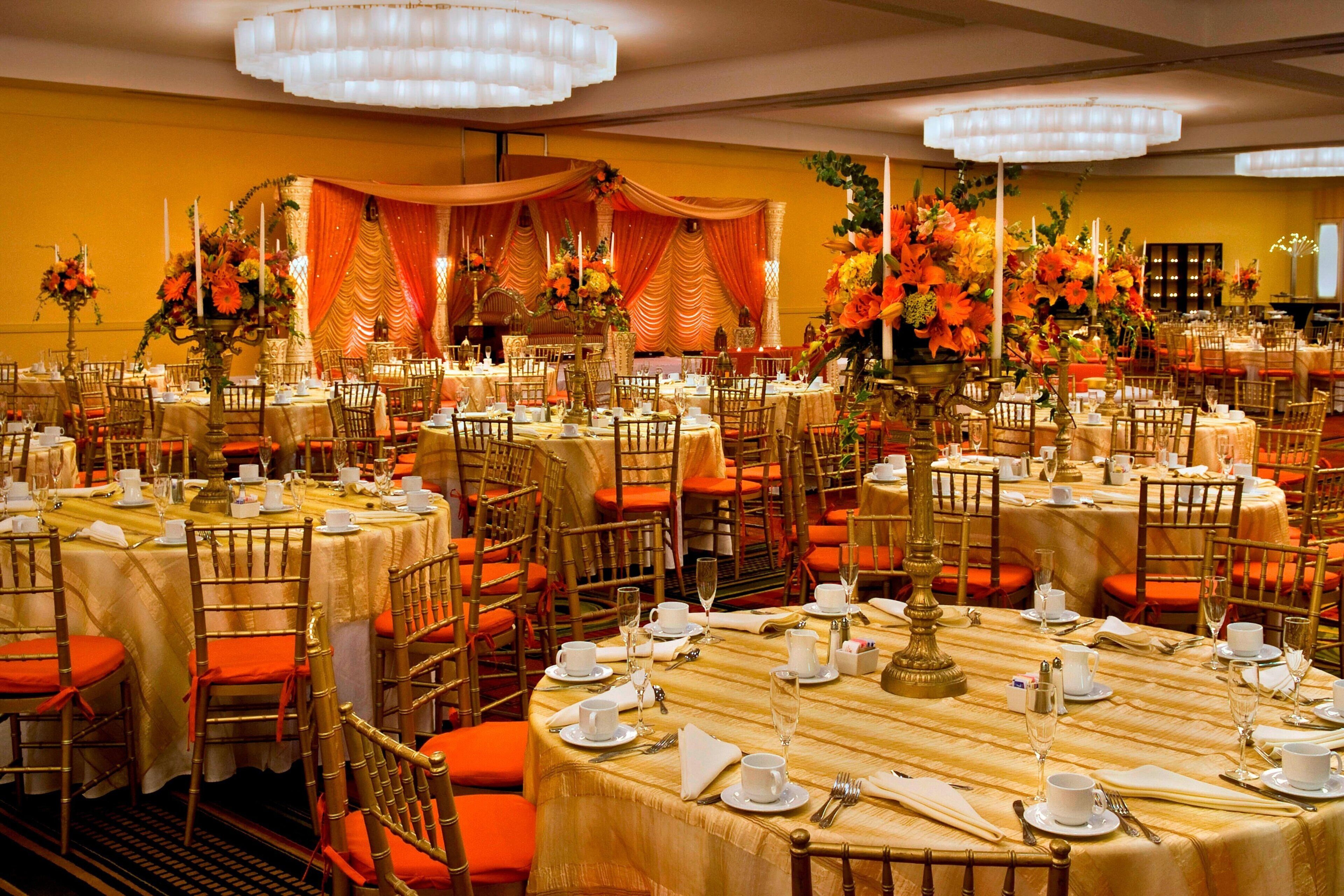 A banquet hall with round tables, gold chairs, and orange cushions.