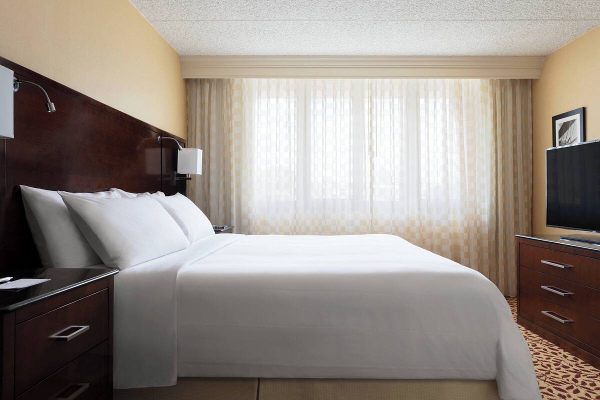 A hotel room with a large bed, a nightstand, a dresser, a television, and a window with curtains.