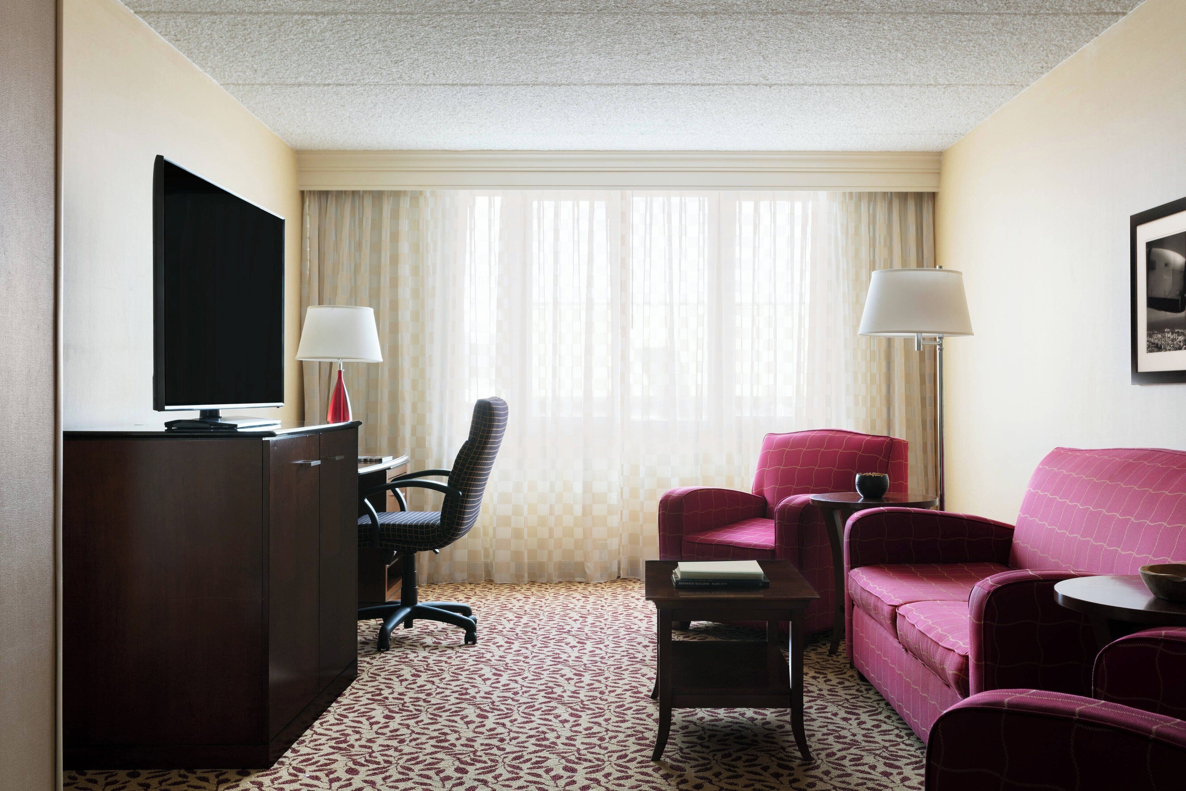 Une chambre d’hôtel équipée d’un bureau, d’une télévision, d’un canapé rouge, d’une chaise et d’une petite table.