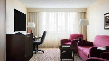 Une chambre d’hôtel équipée d’un bureau, d’une télévision, d’un canapé rouge, d’une chaise et d’une petite table.