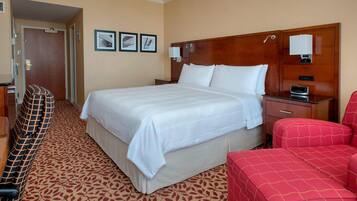 Una habitación de hotel con una cama grande, un sillón rojo, un cabecero de madera y una alfombra estampada.