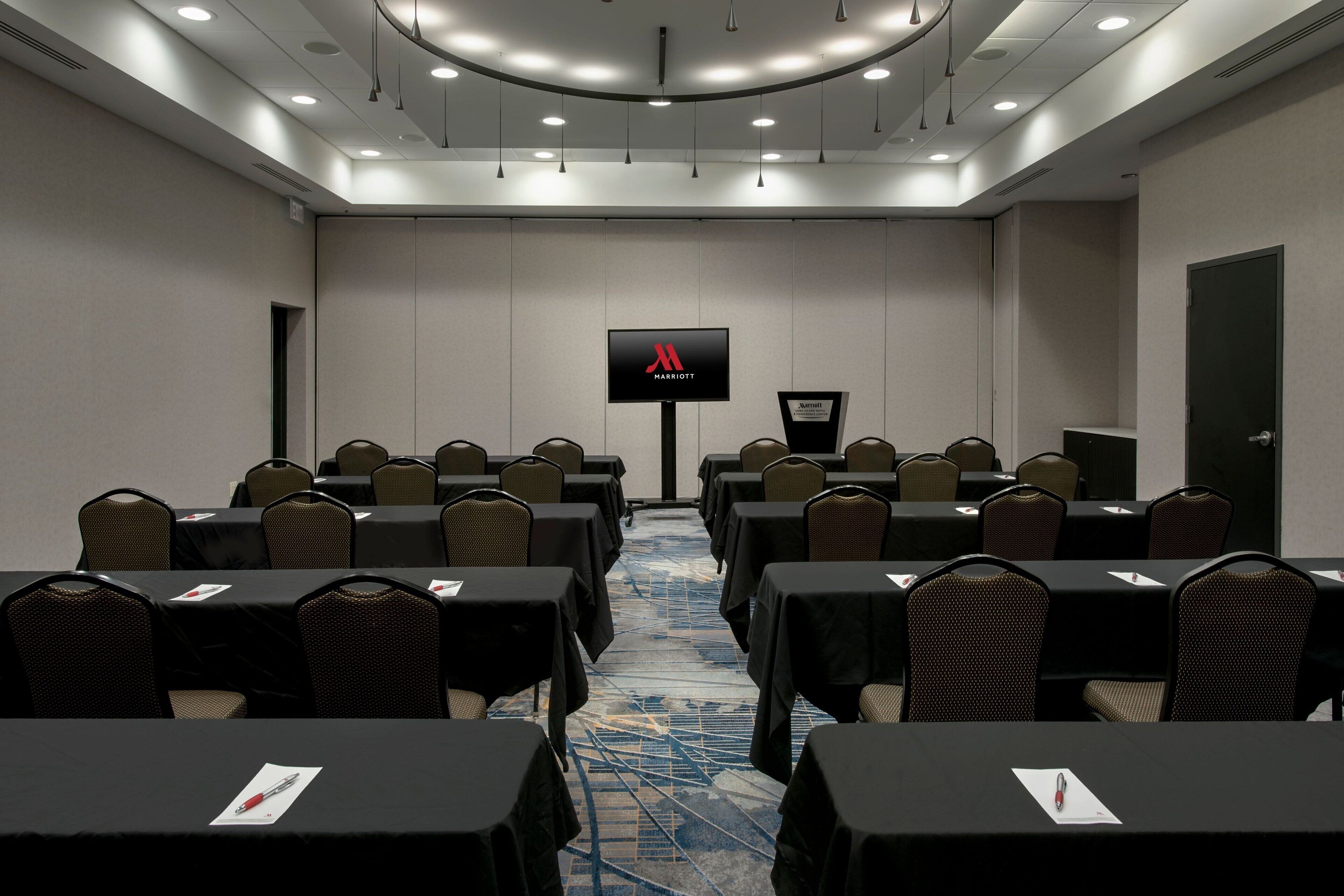 A conference room with tables and chairs, a large screen, and a podium.