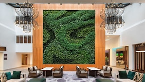 Eine Lobby mit einer großen grünen Wand, Sitzbereichen und modernen Kronleuchtern.