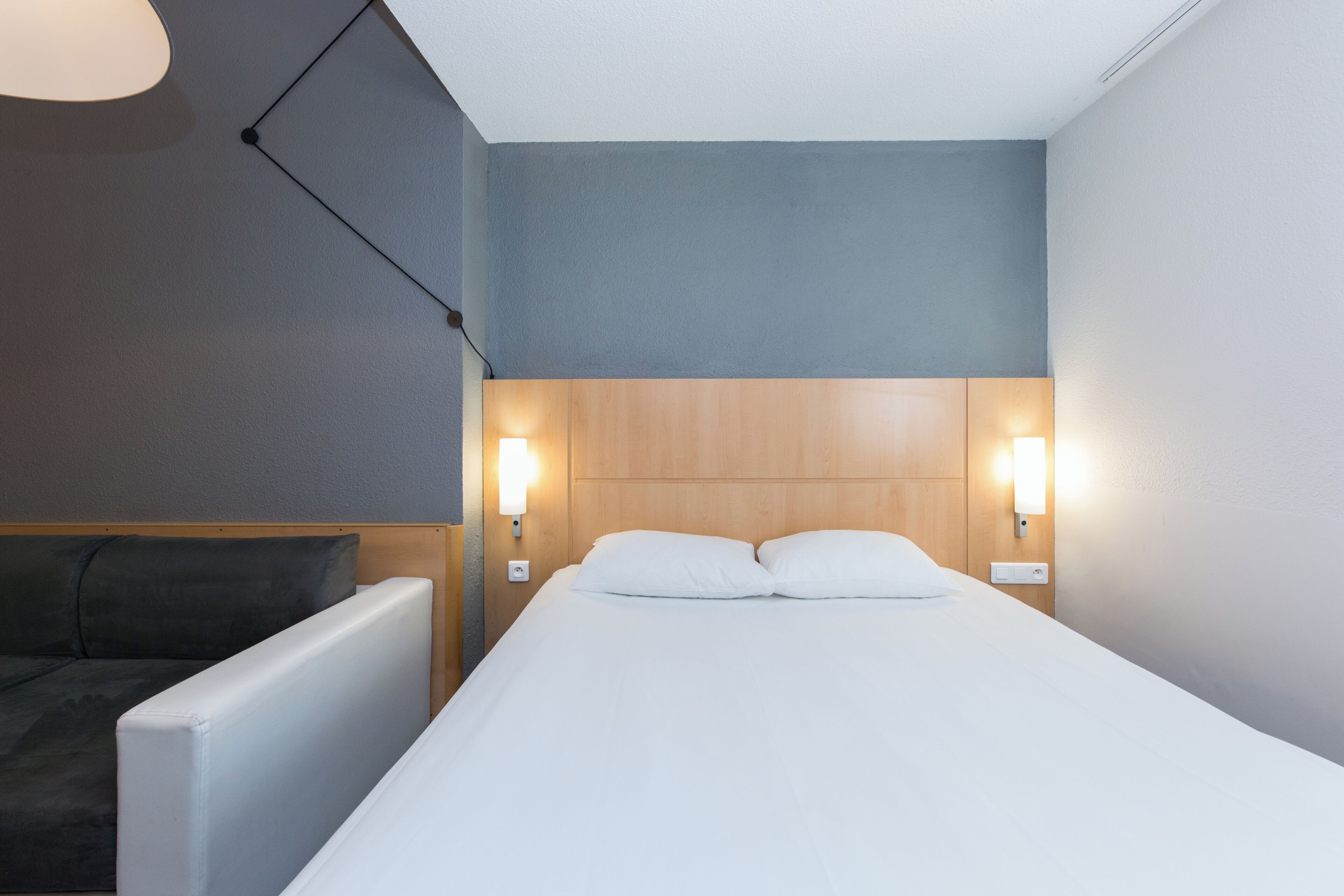 A hotel room with a bed, bedside lamps, a nightstand, and a sofa.