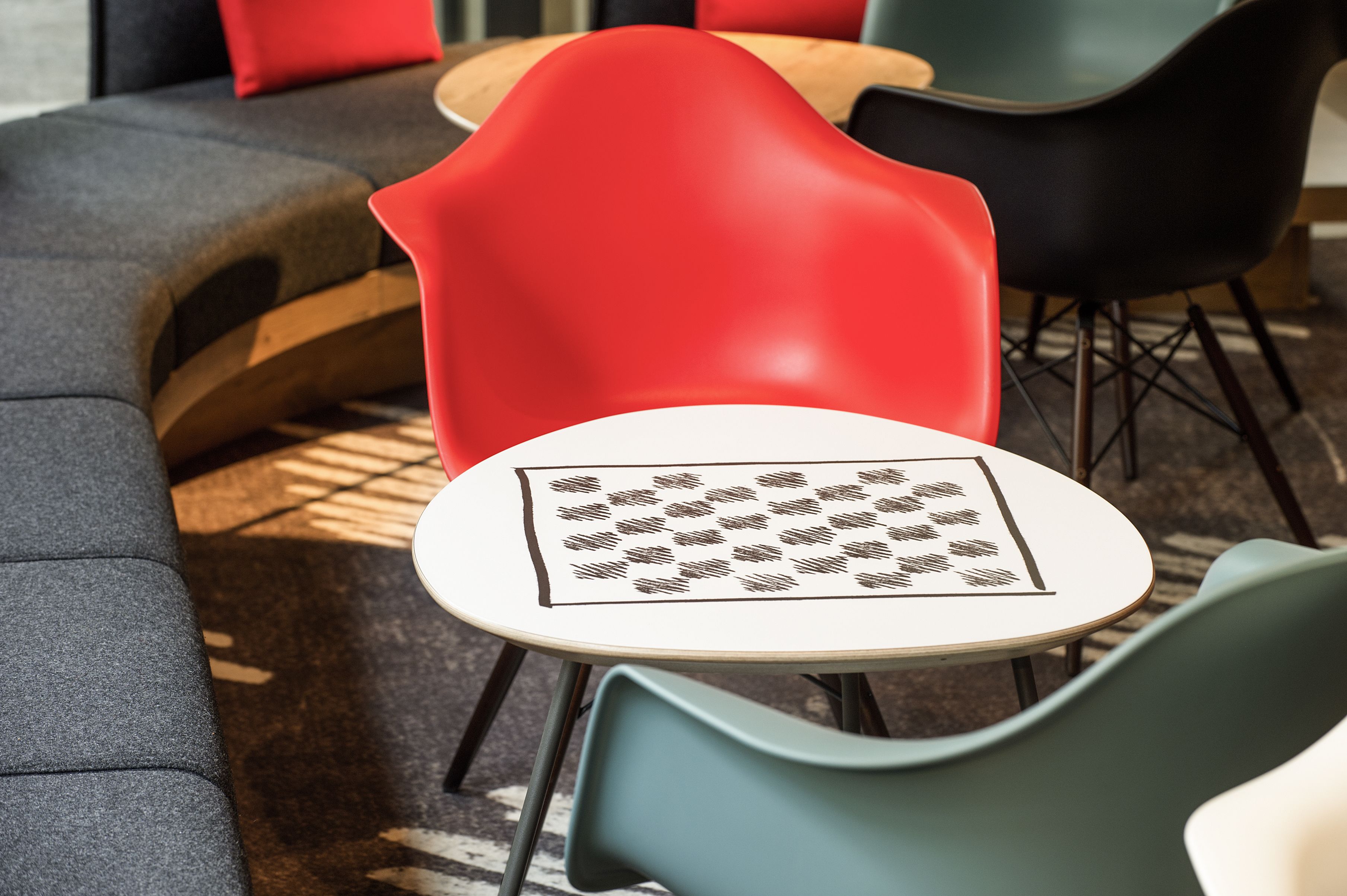 A seating area with a round table, a red chair, and a grey sofa.