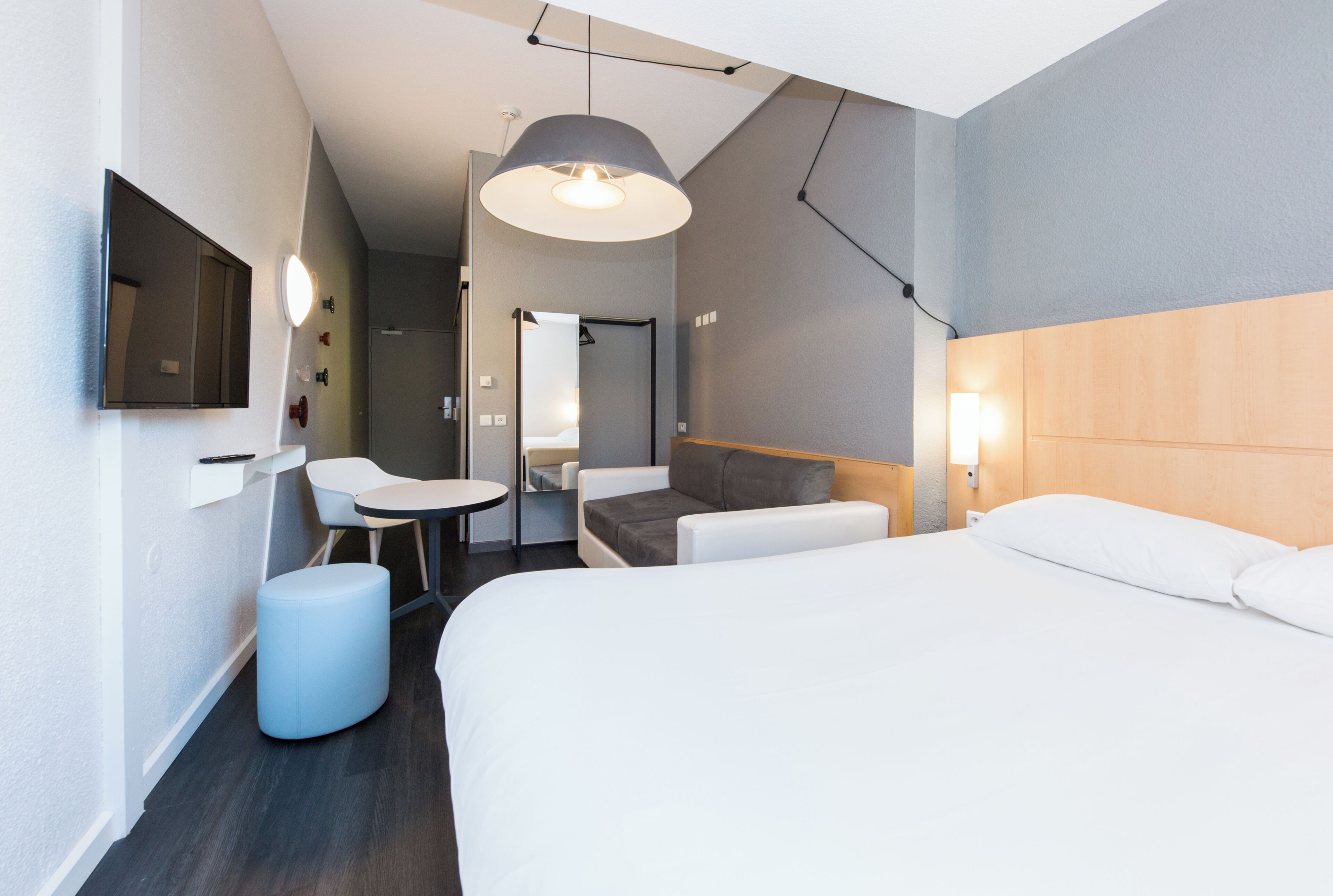 A modern hotel room with a bed, a desk, a chair, and a hanging light fixture.