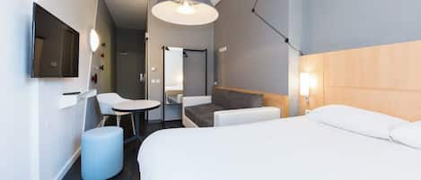 Habitación de hotel moderna con una cama, un escritorio, una silla y una lámpara colgante.