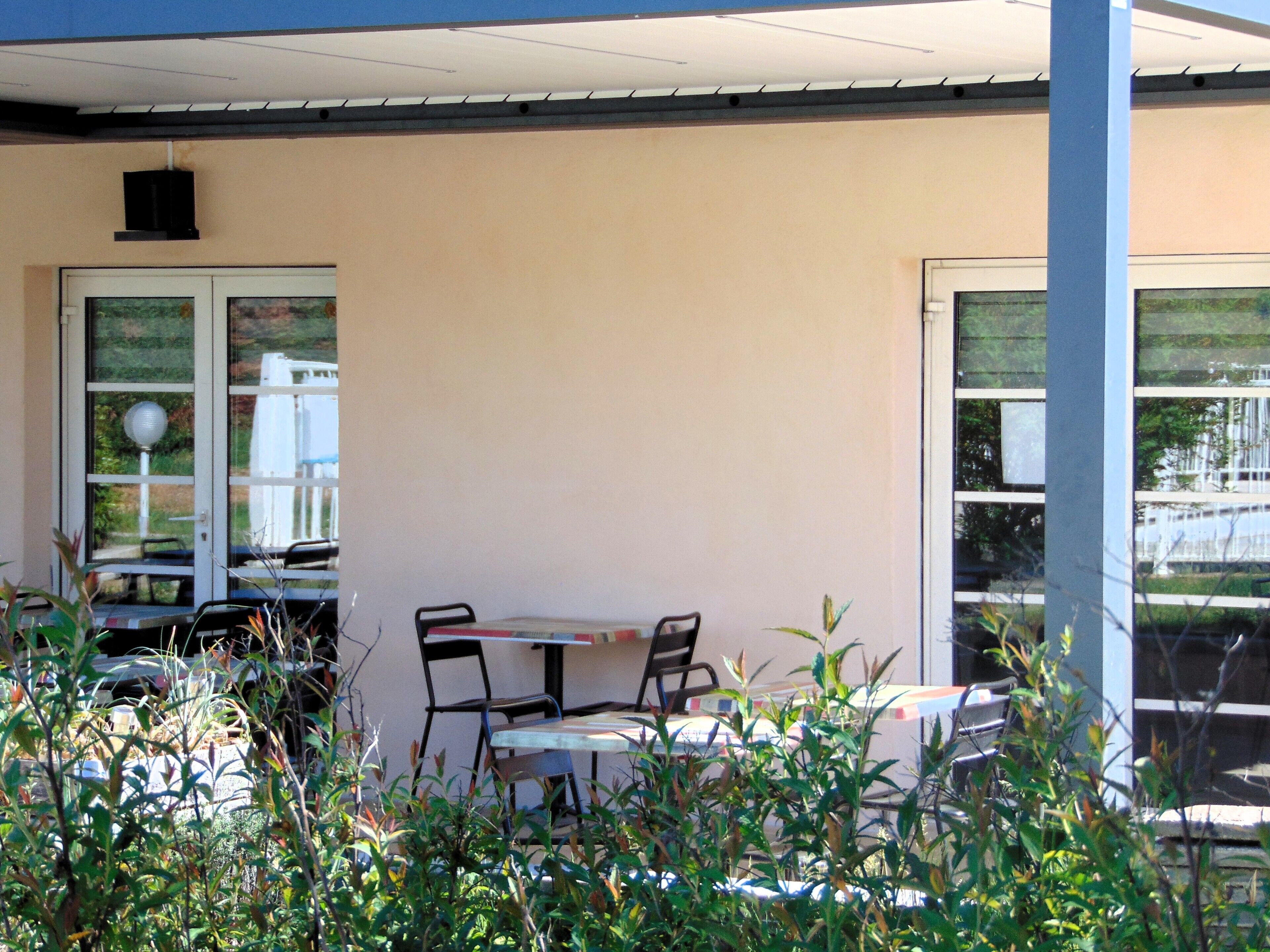 Een terras met tafels en stoelen, een deur en een raam met uitzicht op een gebouw.