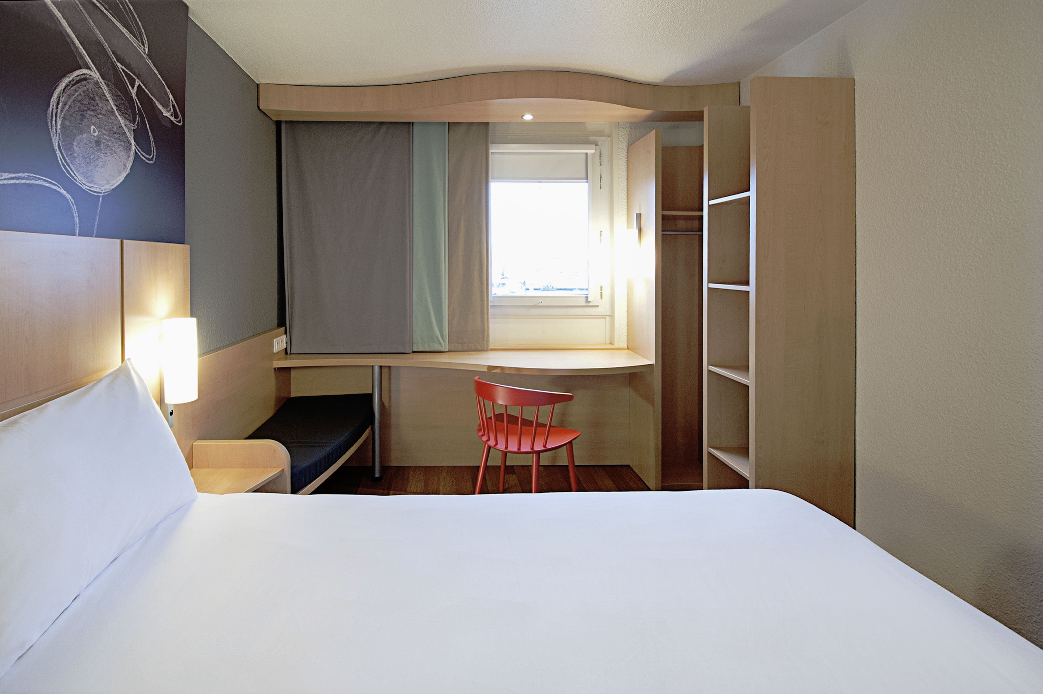 Et hotelværelse med seng, skrivebord, stol, vindue og skab.