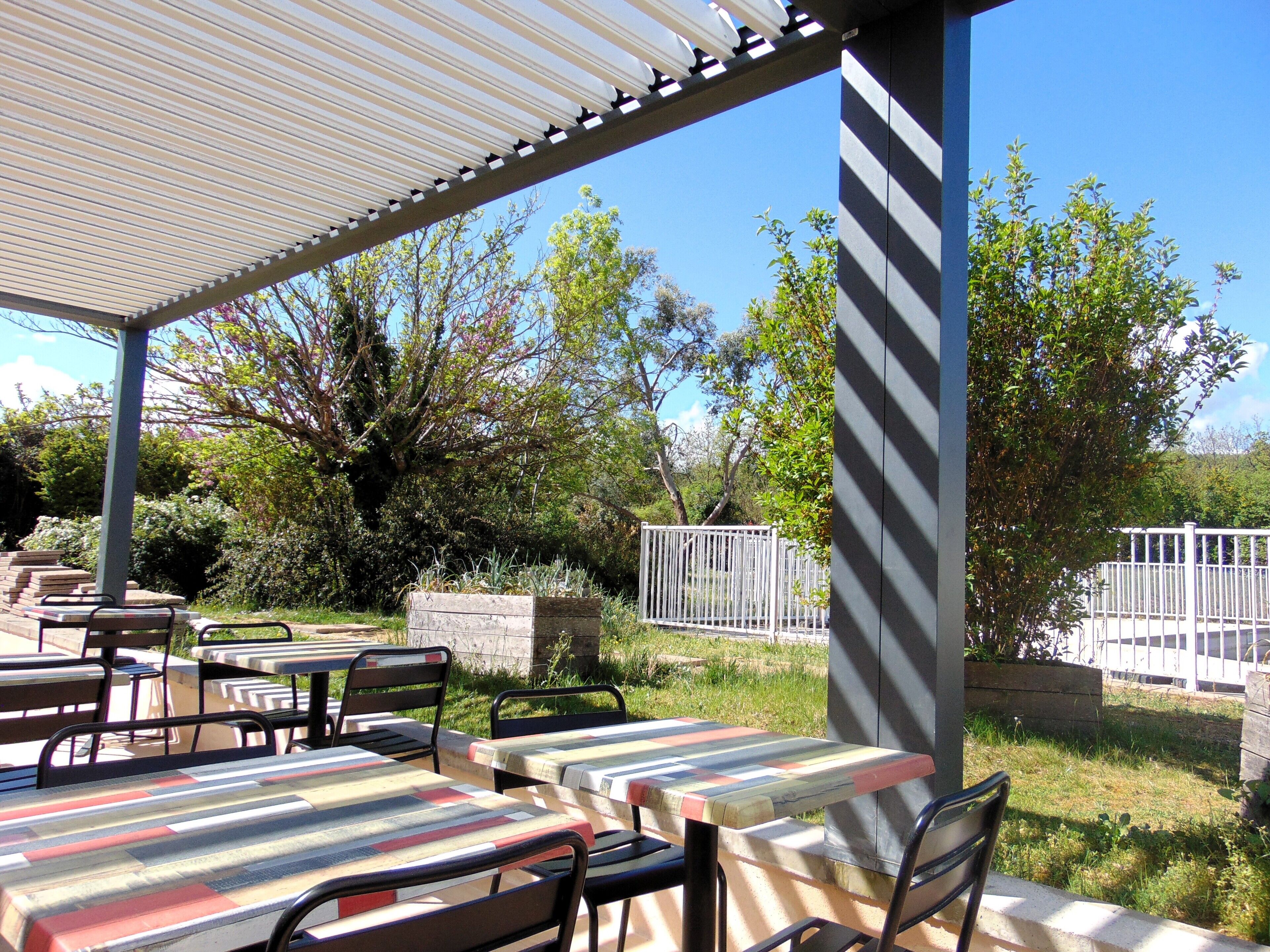 An outdoor patio area with tables and chairs, surrounded by greenery and a fence.