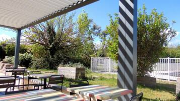 An outdoor patio area with tables and chairs, surrounded by greenery and a fence.