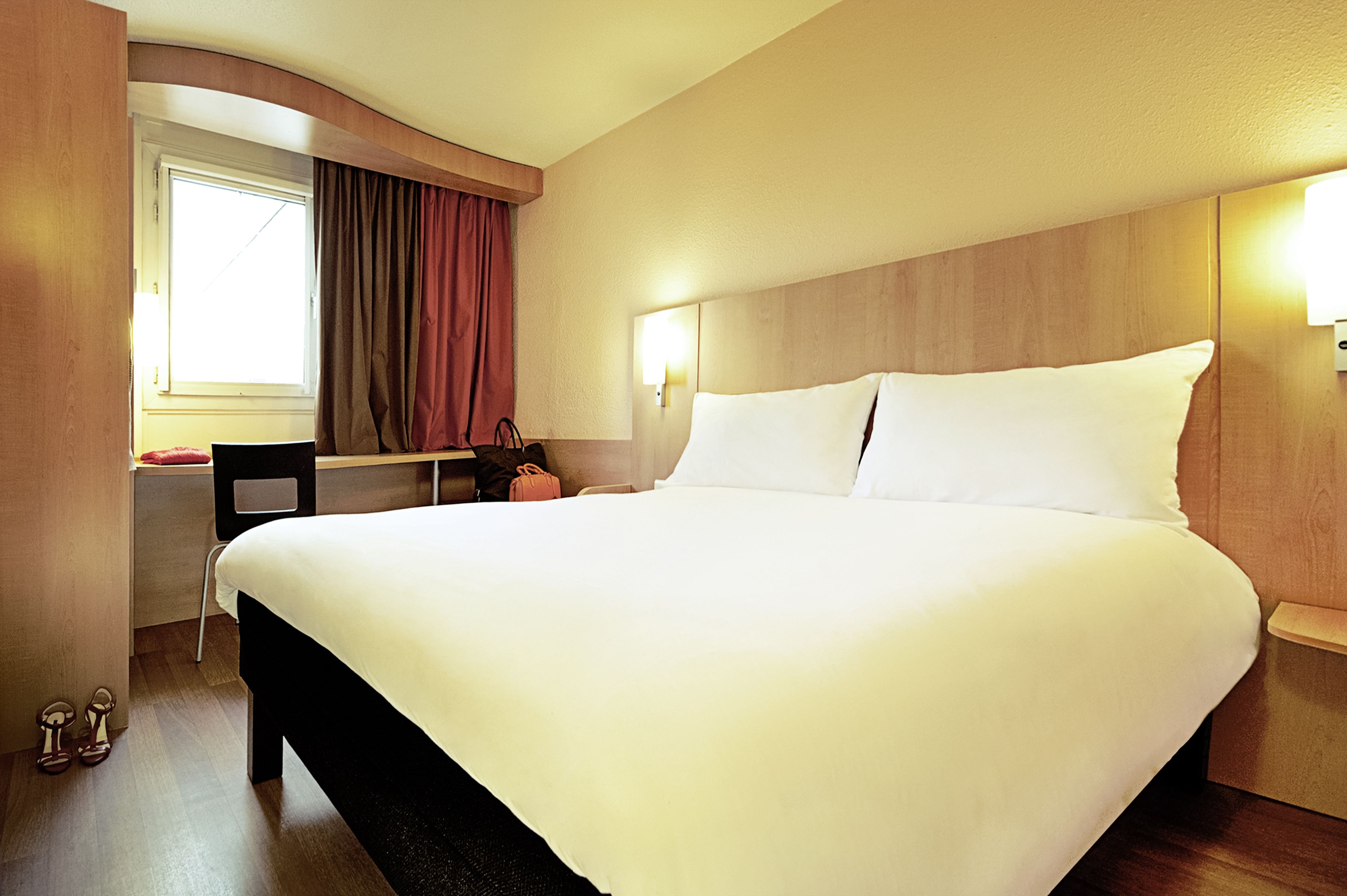 A hotel room with a large bed, a desk, a chair, and a window with curtains.