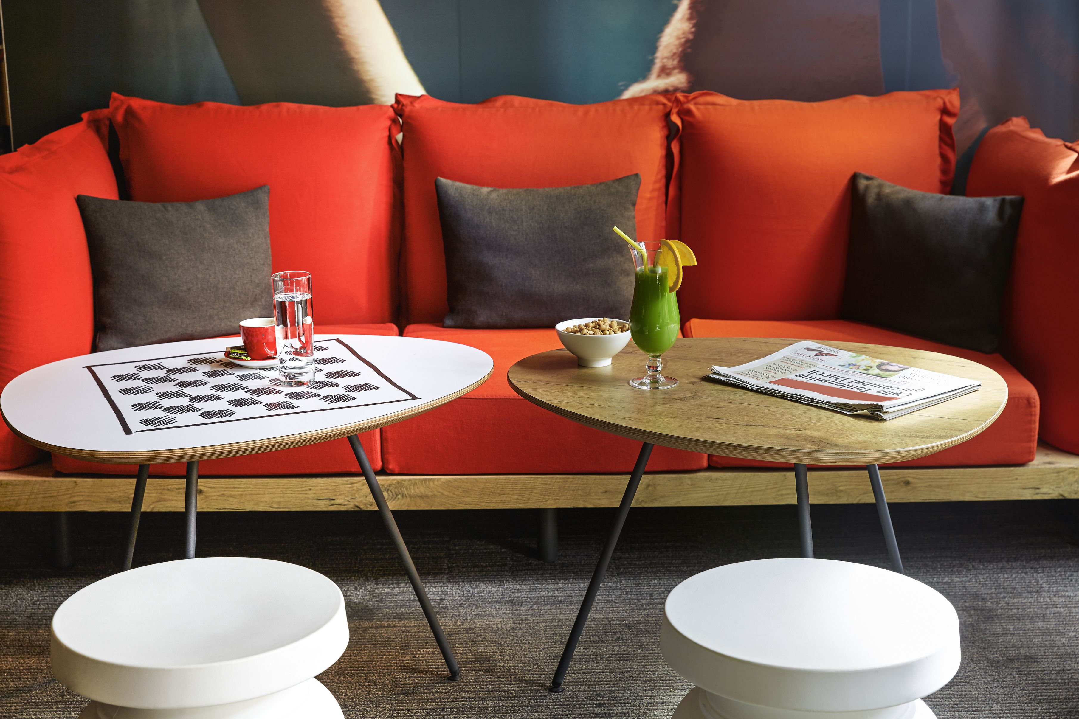 Un salon moderne avec un canapé rouge, deux tables blanches et un magazine.