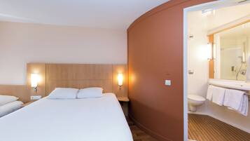 Une chambre d’hôtel avec un grand lit, deux tables de chevet, une lampe fixée au mur et une salle de bain avec douche et toilettes.