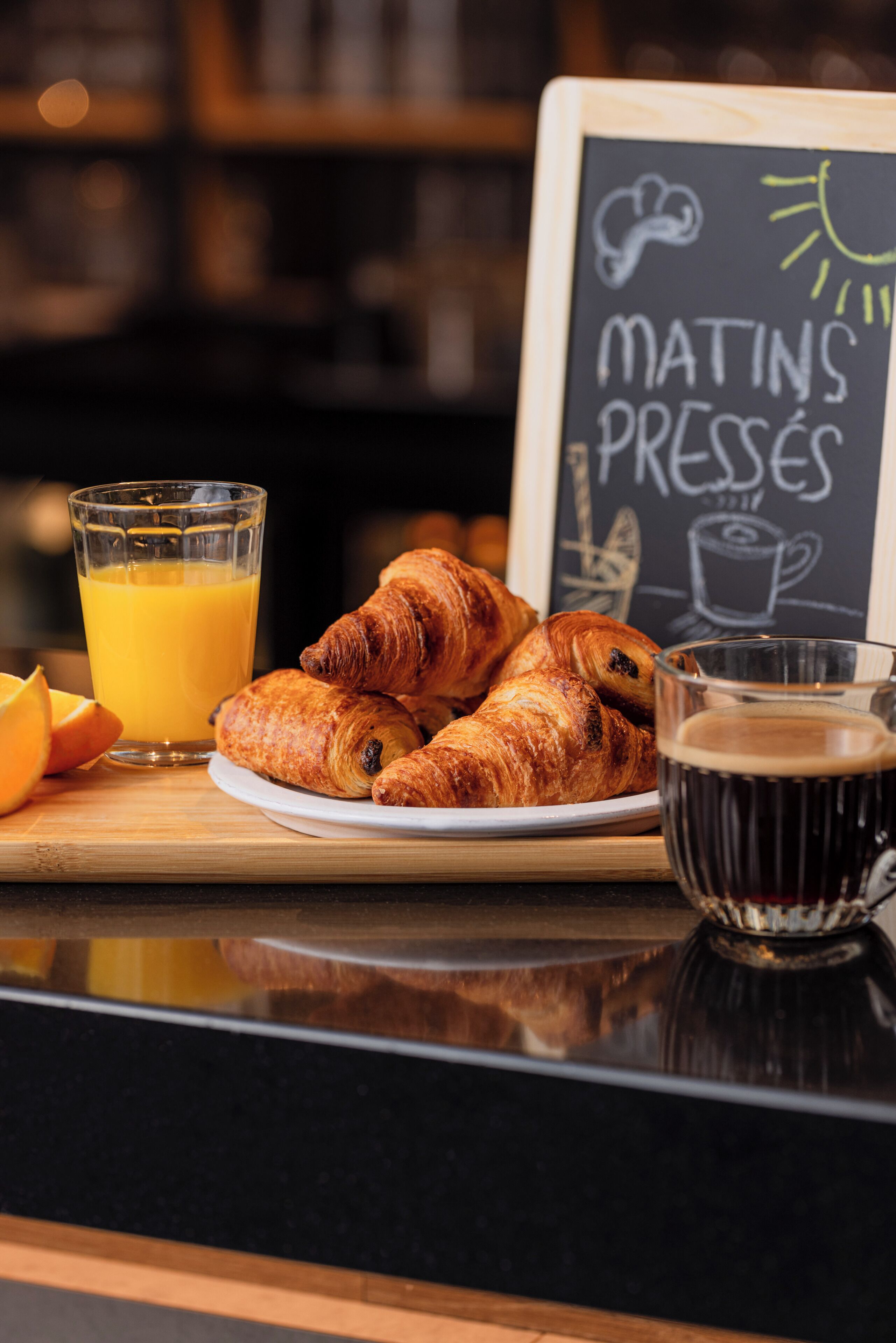 Desayuno con croissants, jugo de naranja y una taza de café sobre una tabla de madera.