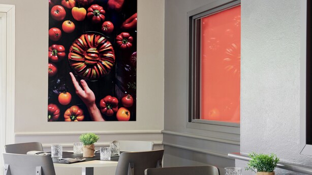 Un comedor con una mesa dispuesta para dos, sillas, una planta pequeña y un cuadro con motivos de frutas.