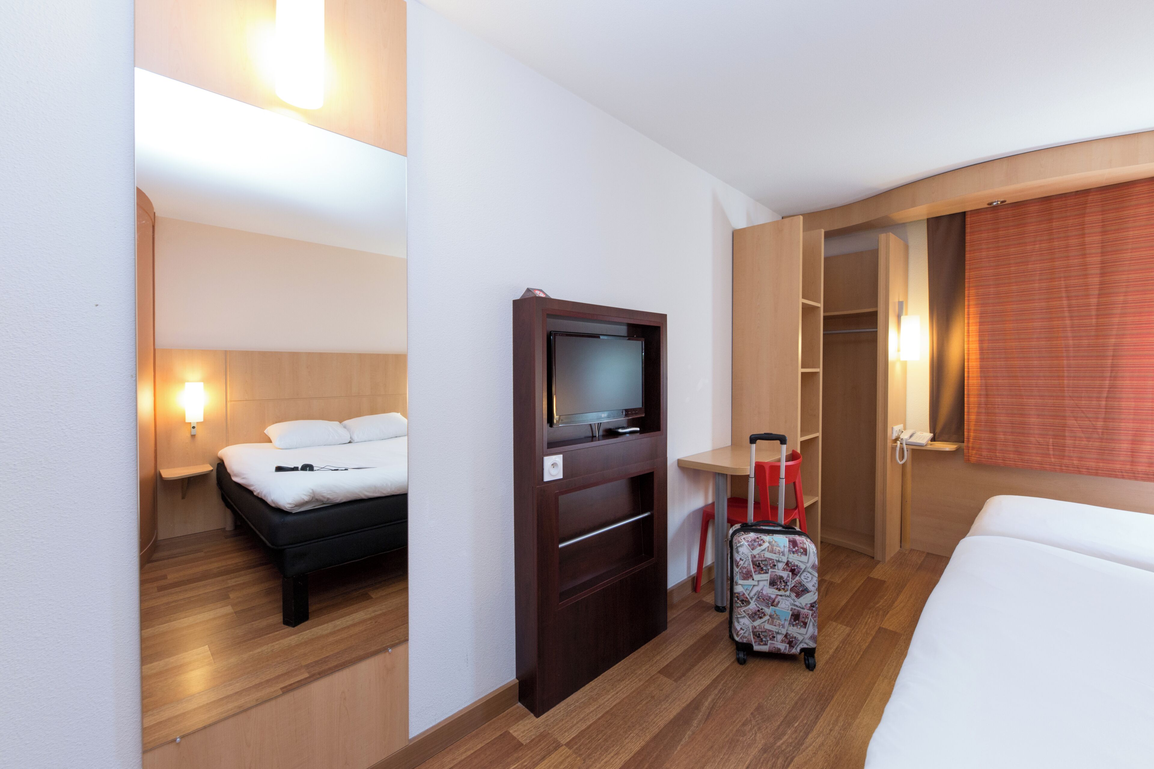 A hotel room with a bed, a TV, a desk, a chair, and a suitcase.
