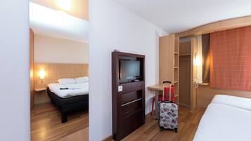 A hotel room with a bed, a TV, a desk, a chair, and a suitcase.