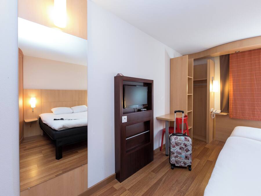 A hotel room with a bed, a TV, a desk, a chair, and a suitcase.