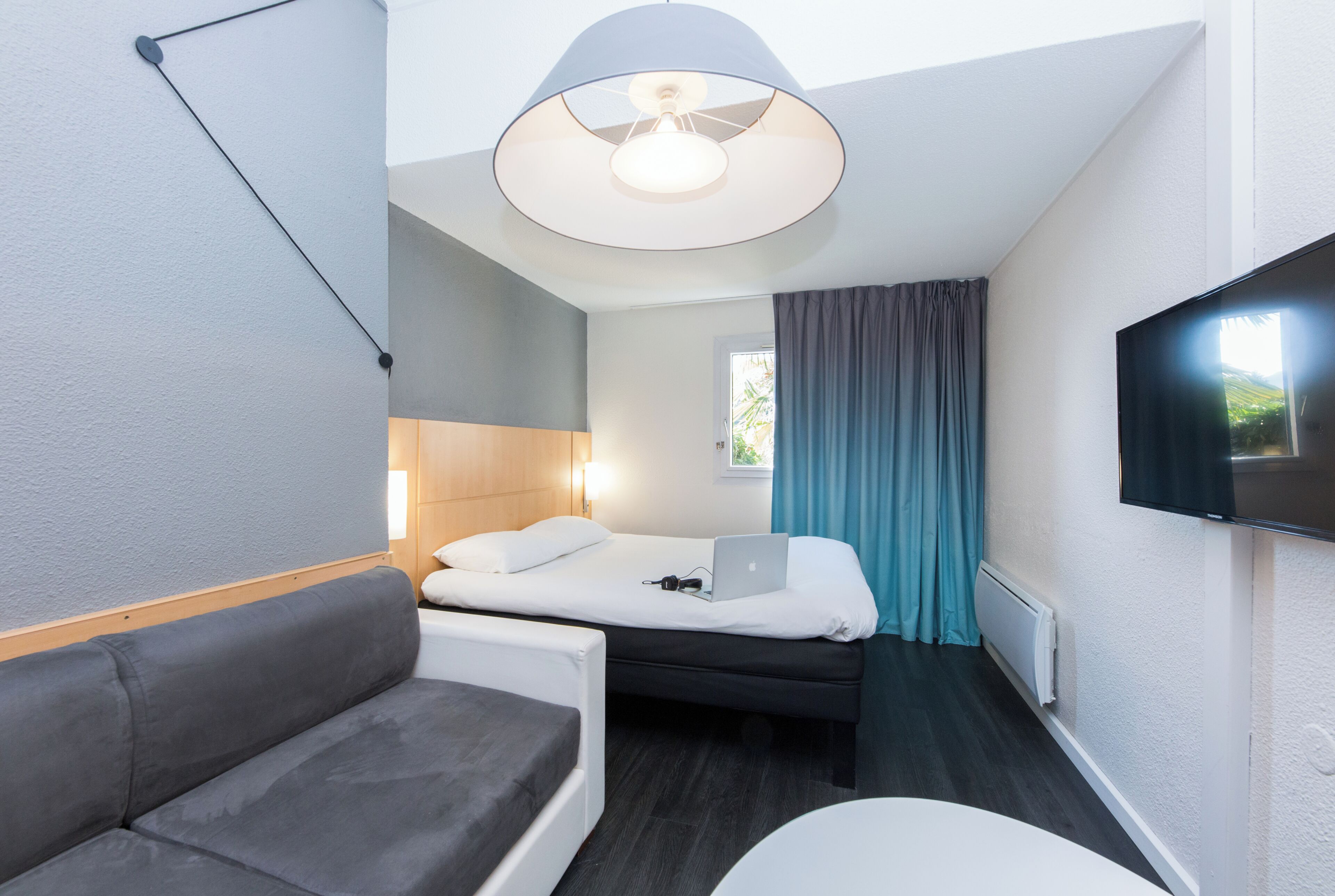 Une chambre d’hôtel de taille réduite, comprenant un lit, un canapé, un bureau et un téléviseur fixé au mur.