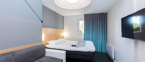 Une chambre d’hôtel de taille réduite, comprenant un lit, un canapé, un bureau et un téléviseur fixé au mur.