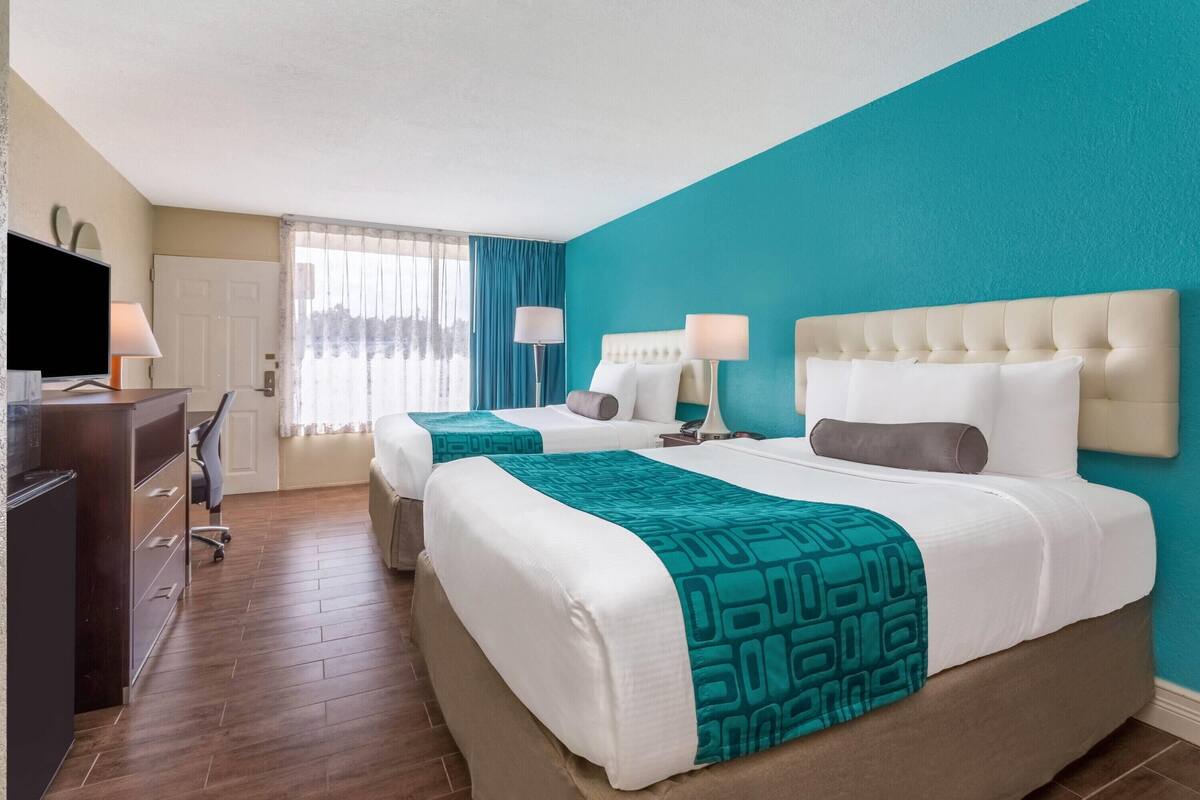 Habitación de hotel con dos camas, un escritorio con computadora y televisor.