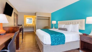 Habitación de hotel con cama, mesitas de noche, escritorio, silla, televisor montado en la pared y baño visible a través de una puerta abierta.