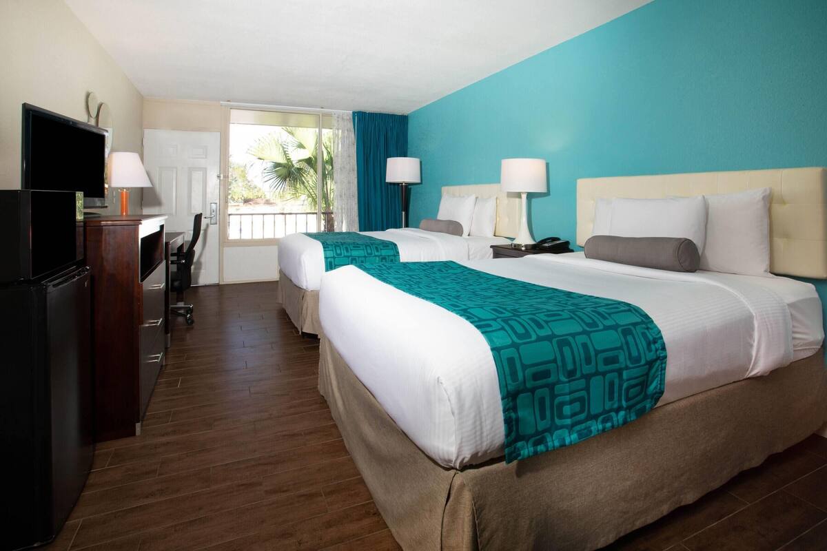 Habitación de hotel con dos camas, un escritorio con computadora y televisor.