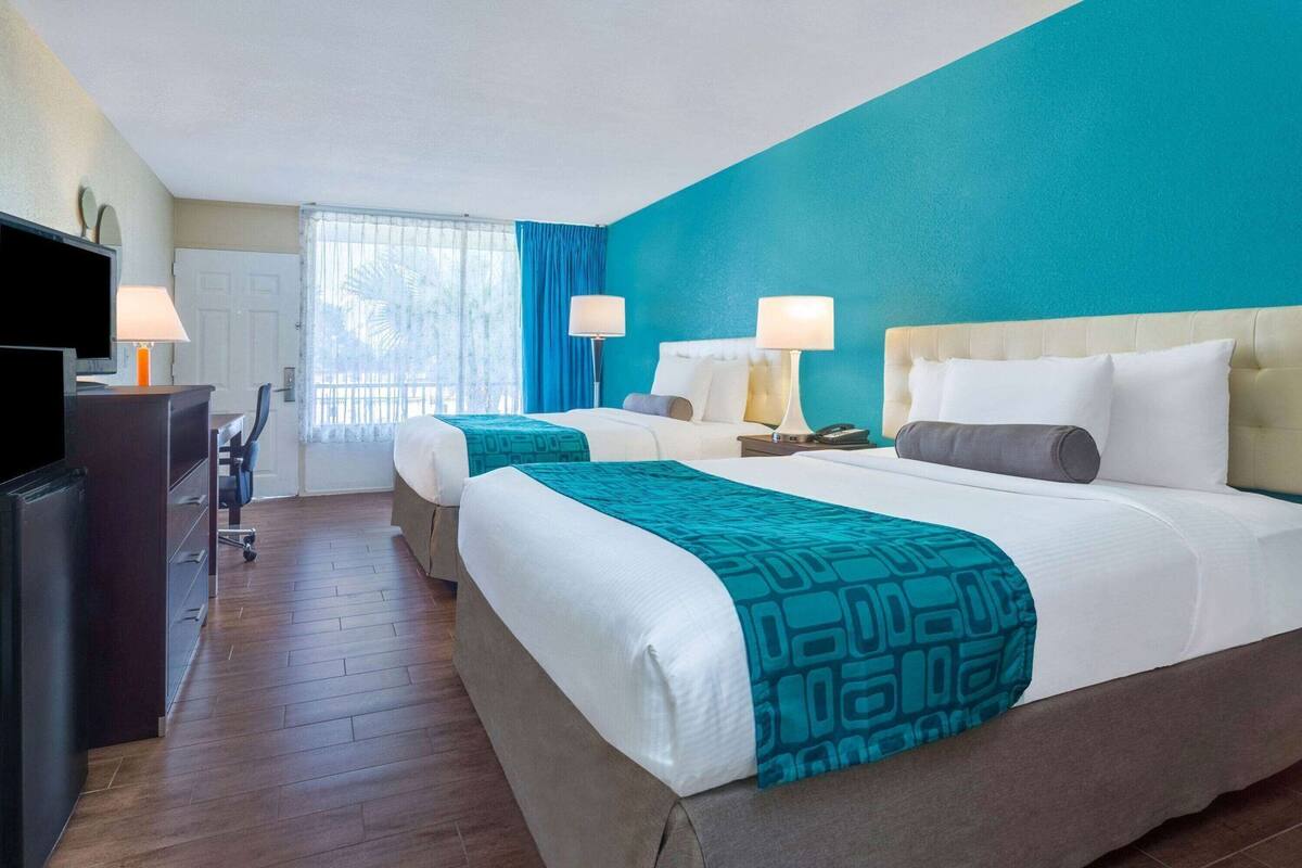 Habitación de hotel con dos camas, un escritorio, un televisor y una ventana con cortinas.