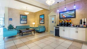 Un vestíbulo con sofás color turquesa, una estación de café y un televisor en la pared.