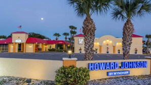 Un hotel Howard Johnson by Wyndham con techo rojo, palmeras y un estacionamiento.