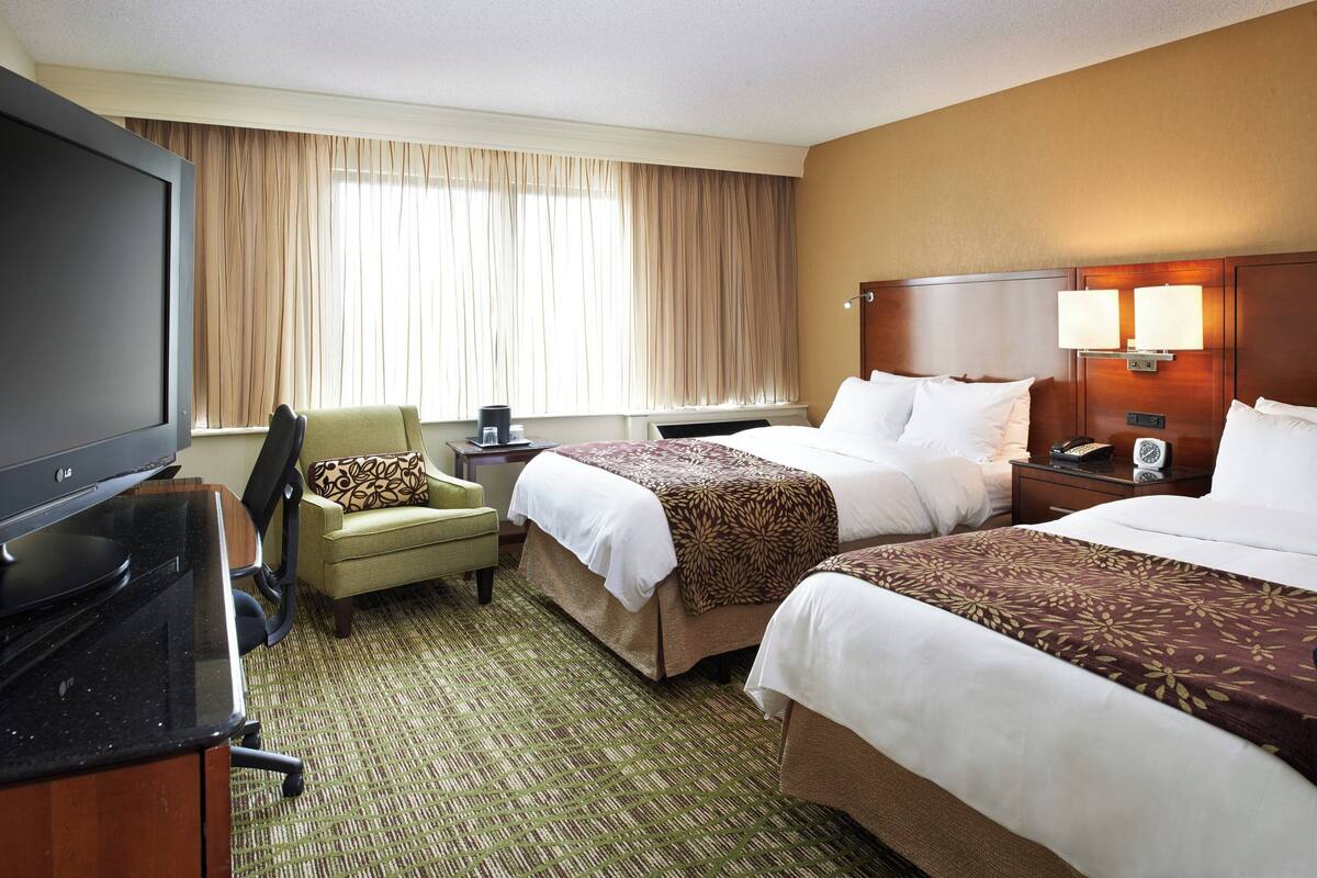 A hotel room with two beds, a TV, a chair, and a desk.