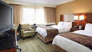 A hotel room with two beds, a TV, a chair, and a desk.