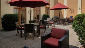Un espace extérieur aménagé en terrasse, avec des meubles en osier, des parasols rouges et un sol carrelé.