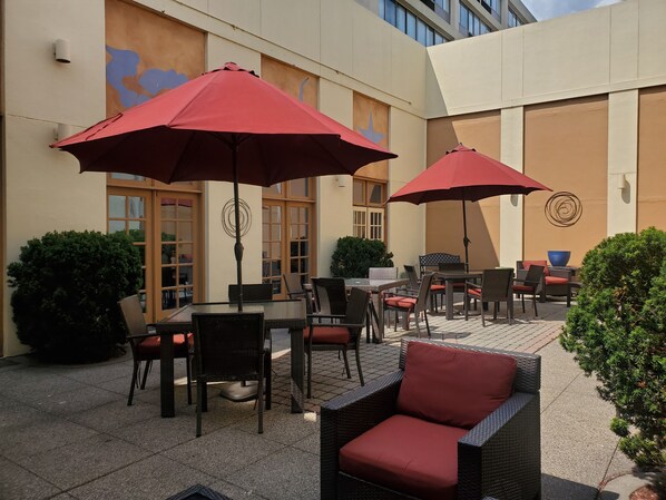 An outdoor patio area with wicker furniture, red umbrellas, and a tiled floor.