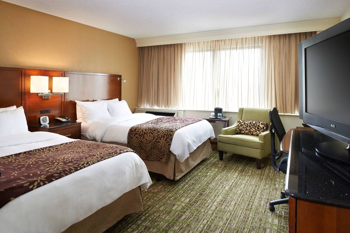 A hotel room with two beds, a television, a desk, and a chair.