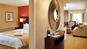 Une chambre d’hôtel avec un lit, un bureau sur lequel se trouve une bouteille de champagne, un miroir et un canapé.