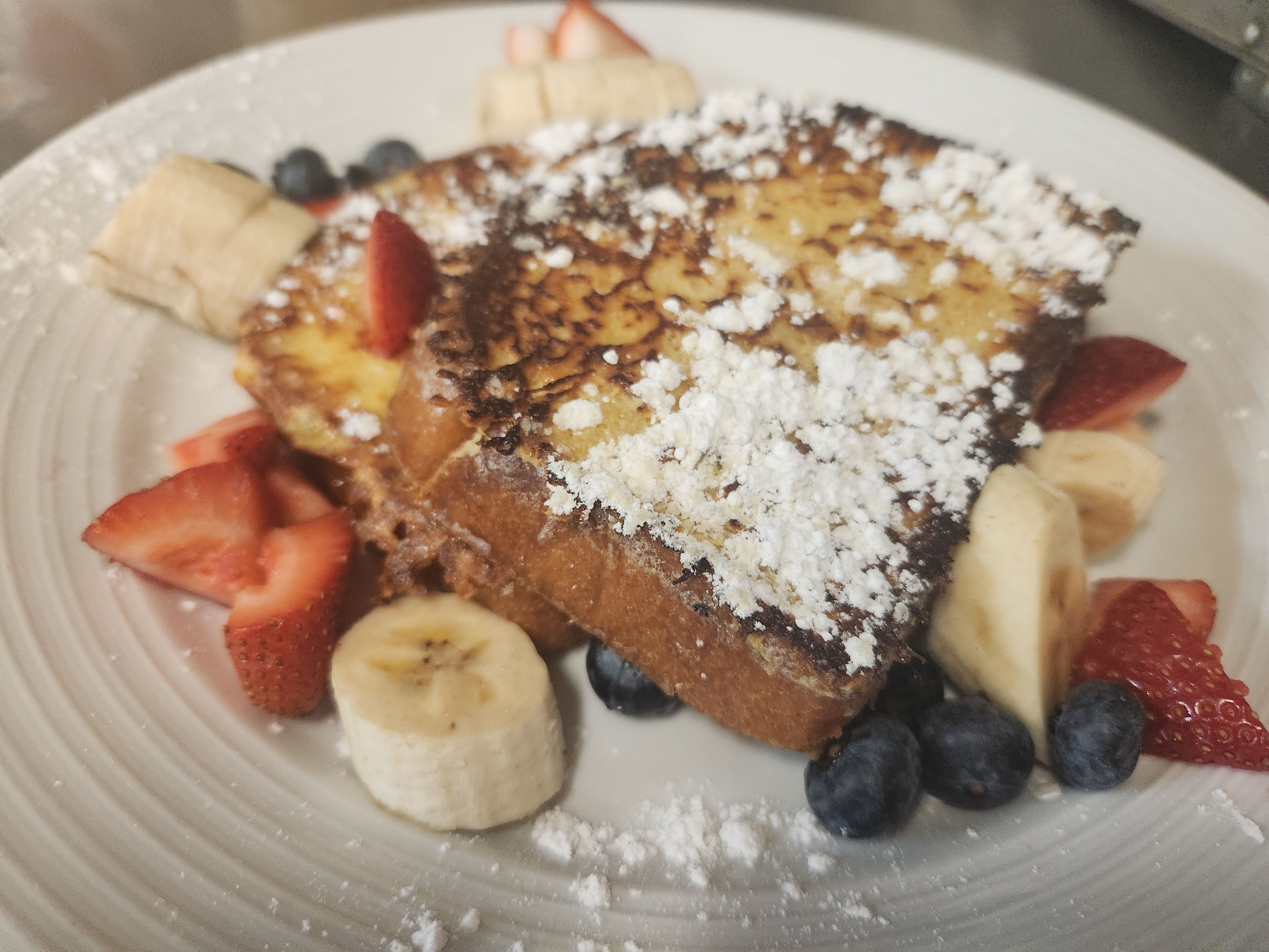 Un plato de tostadas francesas con fresas, plátanos y arándanos.