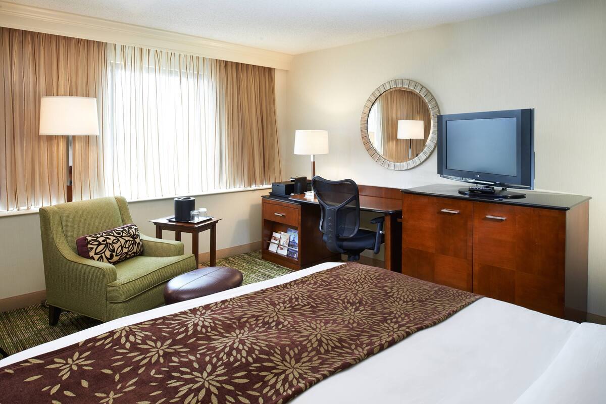 A hotel room with a bed, a desk with a computer, a chair, a television, and a dresser.