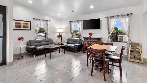 Una sala de estar moderna con sofá, sillón, mesa de comedor y sillas. Hay un televisor montado en la pared y una mesita con una lámpara.