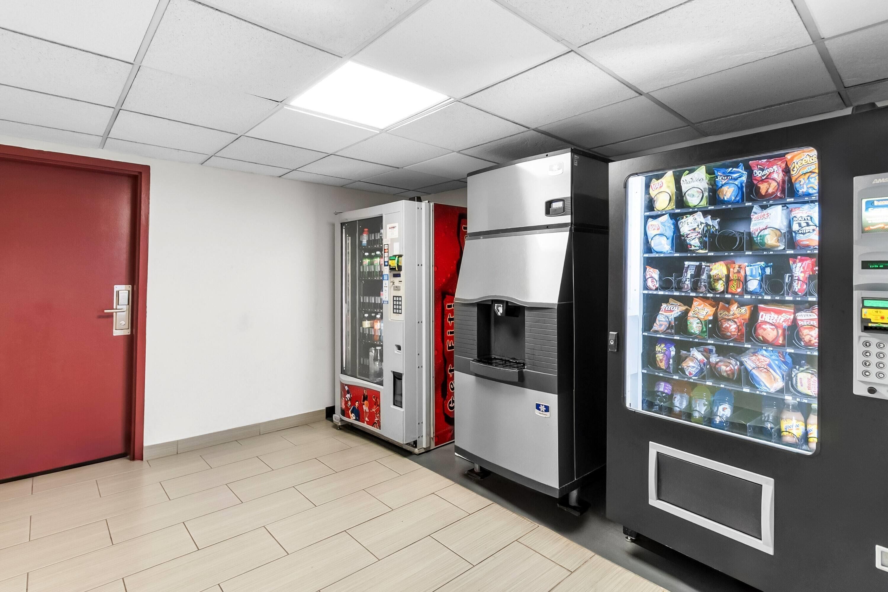 A vending machine area with a red door, a silver refrigerator, and a black vending machine.